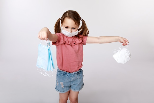 Foto niña con una máscara médica en su rostro sosteniendo muchas máscaras médicas y ffp2