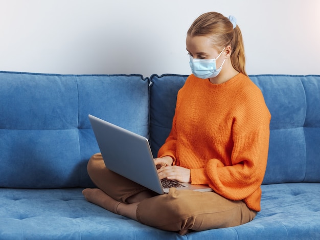 Una niña con una máscara médica trabaja de forma remota en Internet.