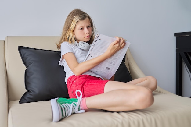 Niña con una máscara protectora médica sentada en el sofá de casa una estudiante que estudia con un cuaderno escolar