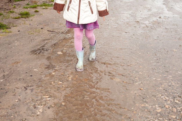 Una niña con medias rosas y botas de goma camina por un arroyo