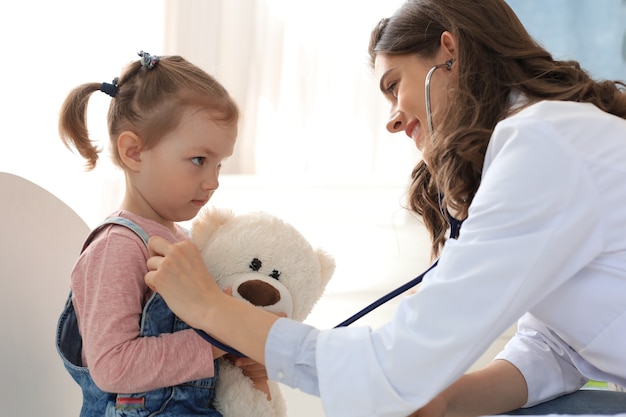 Niña en el médico para un chequeo. La mujer del doctor ausculta los latidos del corazón del niño.