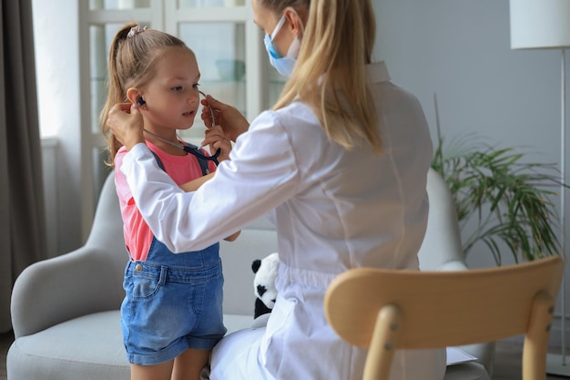 Niña en el médico para un chequeo. El niño ausculta los latidos del corazón del médico.