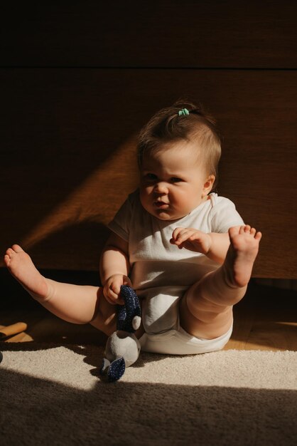 Una niña de un mes está estirando las piernas sobre la alfombra vestida con un mono.