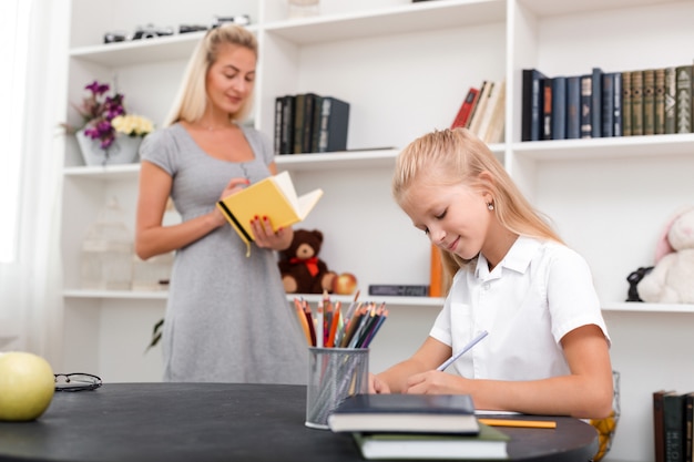 La niña en la mesa hace su tarea, su madre la revisa