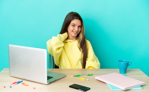 Niña en una mesa con un portátil sobre fondo azul aislado riendo