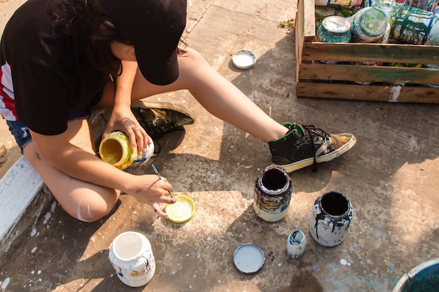 Niña mezclando pintura blanca en una tapa en la calle.