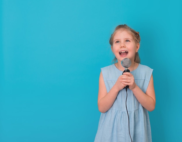 Niña con micrófono cantando sobre fondo azul con espacio de copia