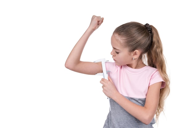 Niña mide sus músculos en su brazo con una pinza de metal, aislado sobre fondo blanco.