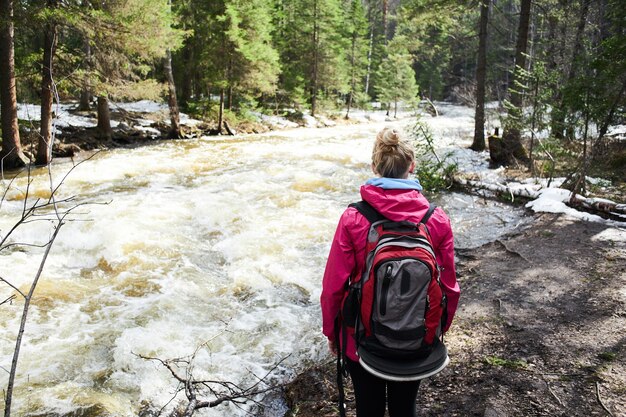 Una niña se para y mira el arroyo de montaña en el bosque.