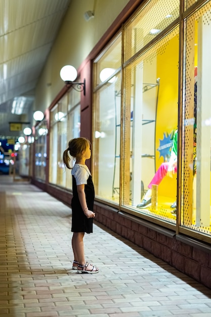 Foto la niña mira el escaparate de cristal grande y quiere comprar algo en las tiendas para niños del escaparate