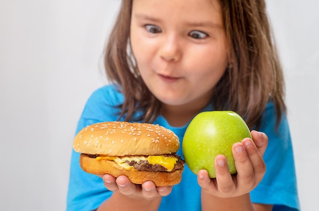 Foto niña mira una hamburguesa y elige entre una hamburguesa con queso y una manzana