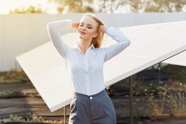 La niña se para y mira el lado derecho cerca de la fila de paneles solares en el suelo con luz solar