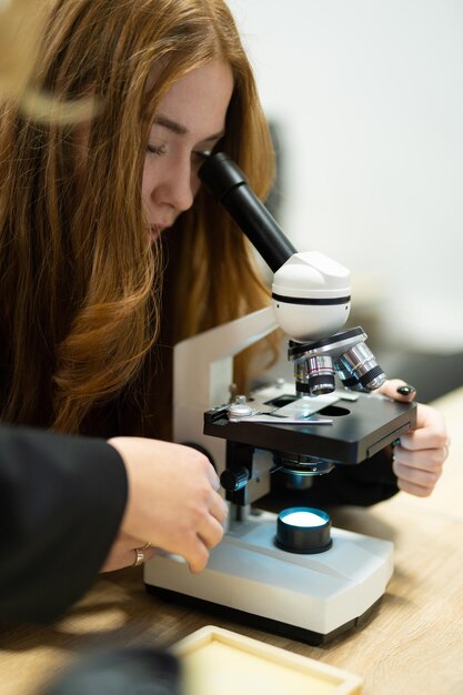 una niña mira en un microscopio profesional en un laboratorio escolar