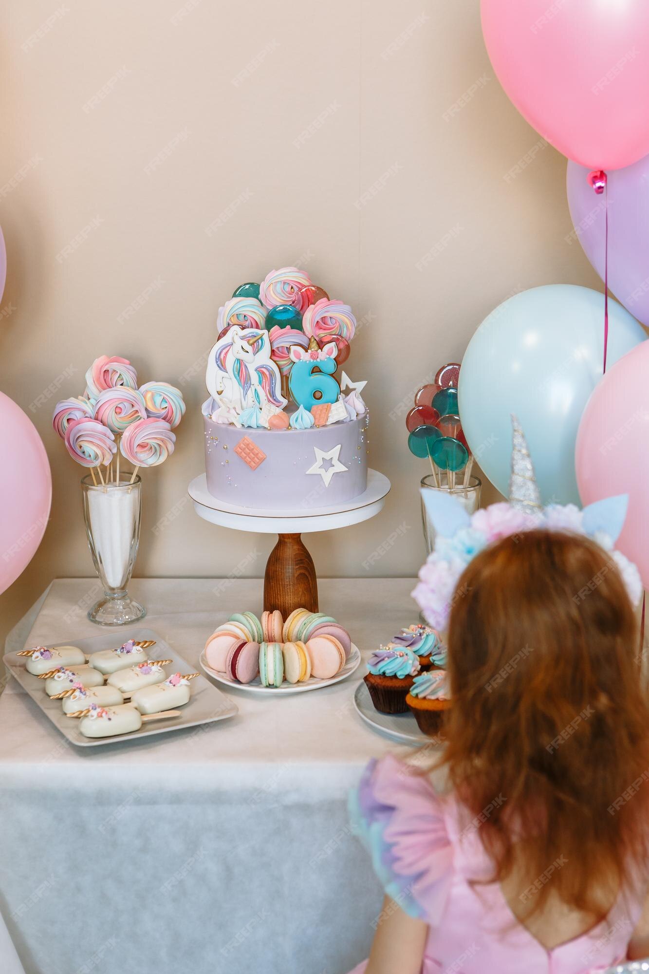 La Nina Mira Su Pastel De Cumpleanos Hecho Con Elementos De Un Unicornio Y Un Arcoiris Las Piruletas Estan Atrapadas En El Pastel Los Pasteles Yacen Junto A El Foto Premium