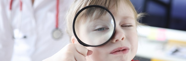 La niña mira a través de la lupa en segundo plano es médico. Encontrar un pediatra para un concepto infantil