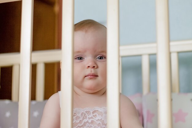 Niña mira a través de los palos en la cama.