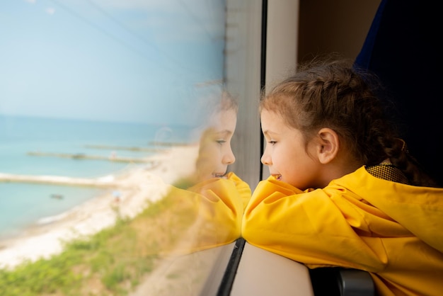 Una niña mira por la ventana de un tren hacia el mar Reflexión Vacaciones Verano Vacaciones en familia