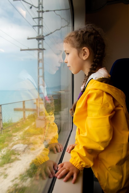 Una niña mira por la ventana de un tren en el mar Viaje Vacaciones Verano Vacaciones familiares