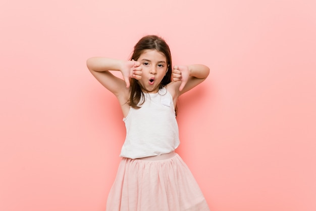 Niña con una mirada de princesa mostrando el pulgar hacia abajo y expresando disgusto.