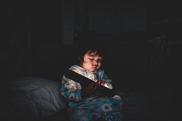 Niña mirando a la cámara mientras está sentada en la cama en casa