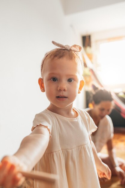 Niña mirando la cámara con su madre al fondo