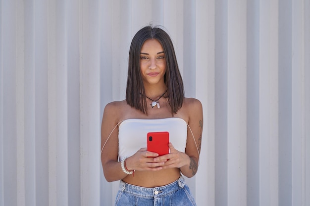 Niña mirando a la cámara con un teléfono inteligente rojo en sus manos