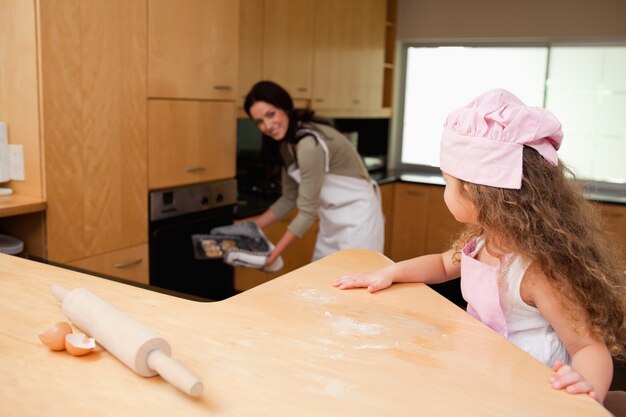 Niña mirando a su madre poniendo galletas en el horno