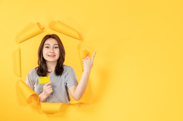 Niña mirando a través de un agujero con tarjeta de crédito en fondo amarillo venta de dinero