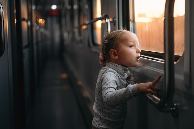 Niña mirando a través de la ventana del tren al atardecer