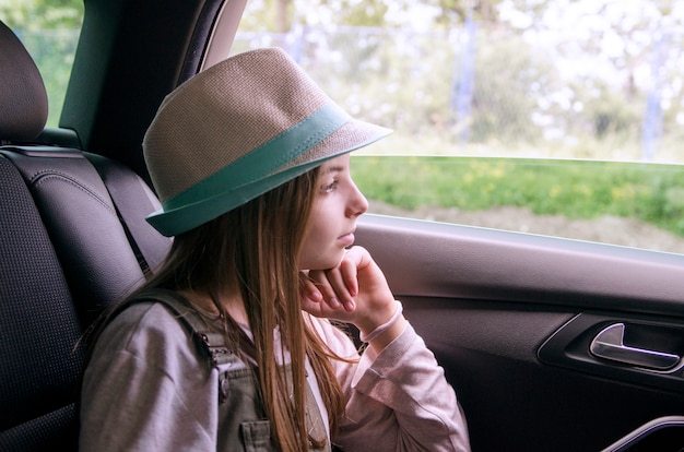 Niña mirando por la ventana del automóvil durante el viaje de fin de semana.Niña viajando a la aldea, mirando la vista desde el interior del automóvil