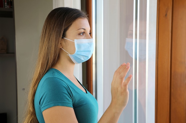 Niña mirando por la ventana usando una máscara contra la enfermedad por coronavirus 2019.