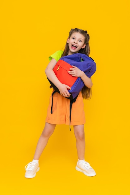 Una niña con una mochila escolar Un niño en pantalones cortos de verano va a cursos educativos Un niño feliz con una cartera Una colegiala de cuerpo entero sobre un fondo amarillo aislado