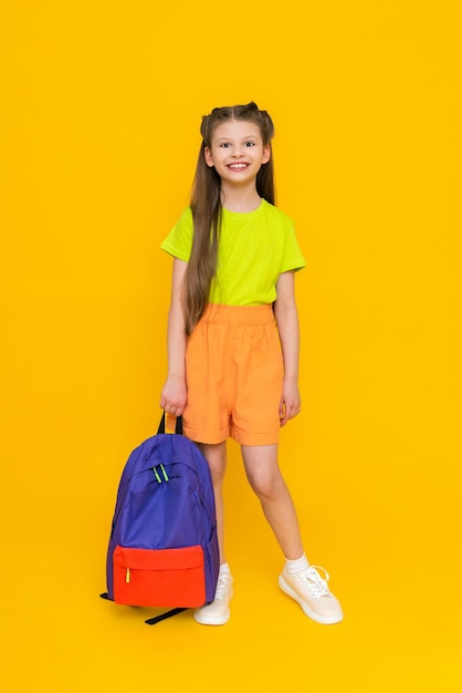 Una niña con una mochila escolar Un niño en pantalones cortos de verano va a cursos educativos Un niño feliz con una cartera Una colegiala de cuerpo entero sobre un fondo amarillo aislado