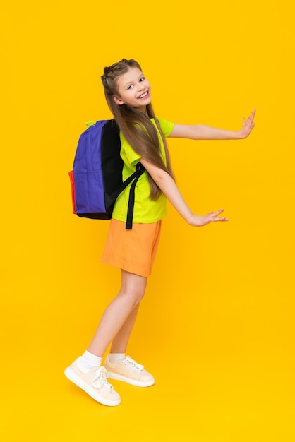 Una niña con una mochila escolar Un niño en pantalones cortos de verano va a cursos educativos Un niño feliz con una cartera Una colegiala de cuerpo entero sobre un fondo amarillo aislado