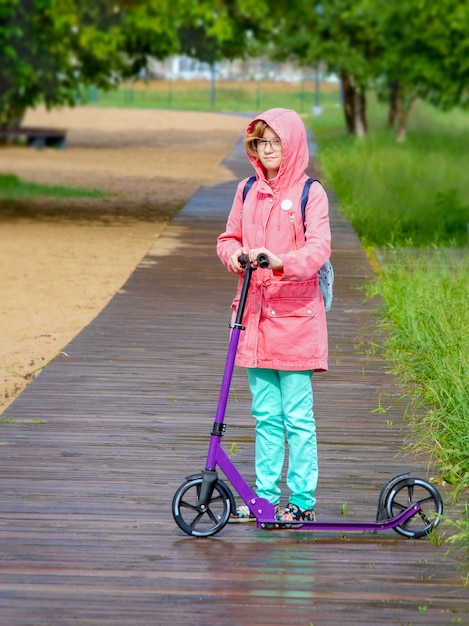 Niña con una mochila en la espalda monta una moto en un parque de la ciudad