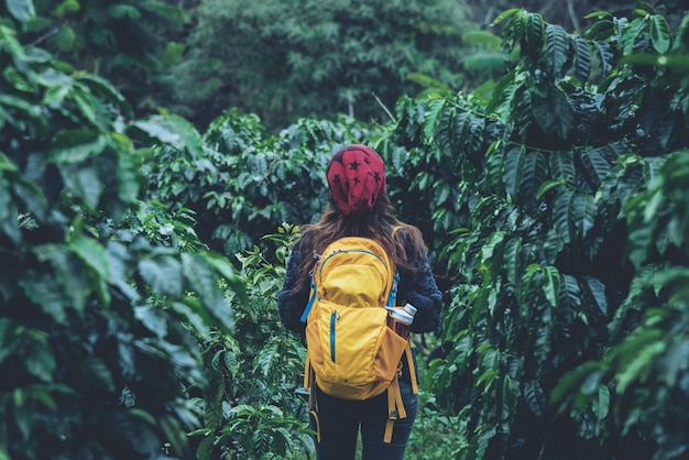 La niña con mochila está de pie y caminando en el jardín de café.