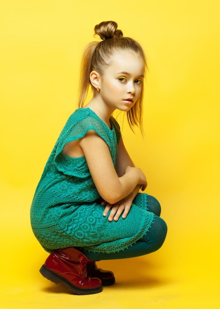 Niña de moda con cabello rubio posando sobre fondo amarillo