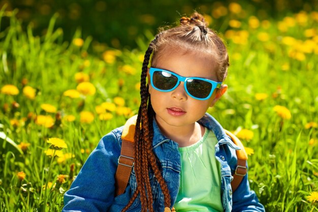 Niña de moda sentada en gafas de sol en la hierba en la naturaleza