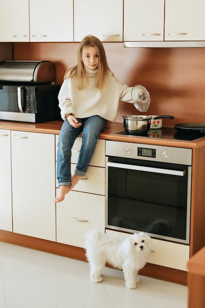 Foto niña modelo juega con mascota perro blanco colegiala maltesa en casa estilo de vida en cocina beige