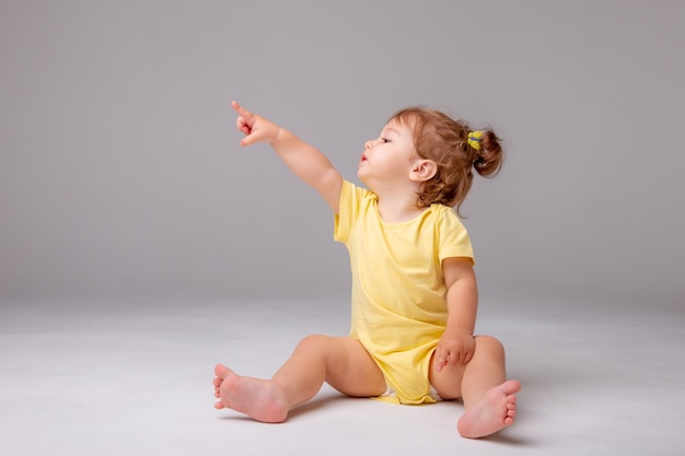 Niña con mono amarillo sentado sobre un fondo blanco.