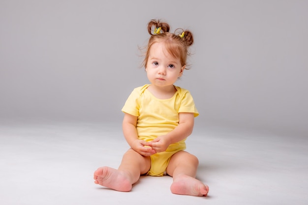 Niña con mono amarillo sentado sobre un fondo blanco.