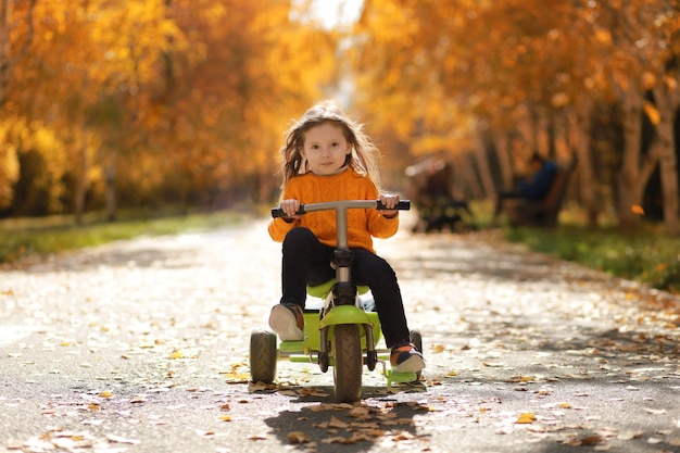 Niña monta una bicicleta de 3 ruedas en el parque de otoño