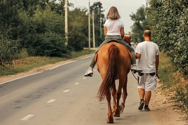 Una niña monta a caballo acompañada por su padre en el caluroso verano