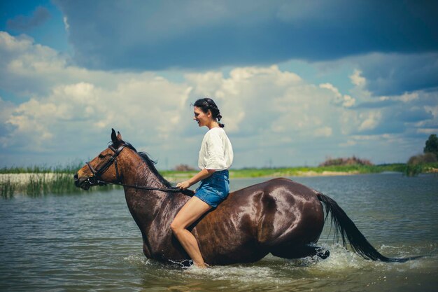 Una niña monta un caballo marrón en el agua del lago