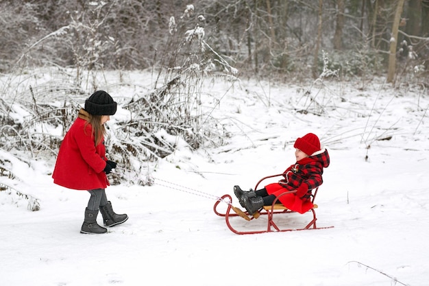 Una niña monta a su hermana en un trineo en el bosque en un día helado de invierno con nieve