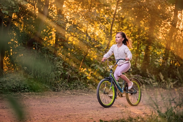 Foto niña montando en bicicleta por un camino rural en la naturaleza al atardecer