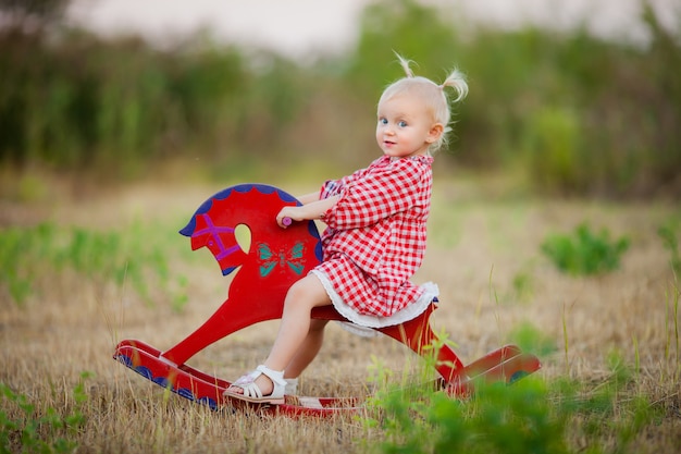 Niña montando un caballo de juguete para pasear en el verano