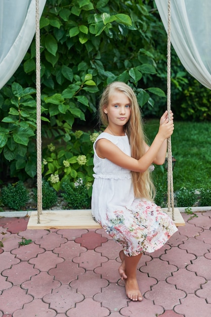 Niña montando un columpio en el verano en el jardín