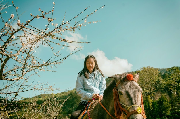 Foto niña está montando en pony marrón en el parque en estilo vintage