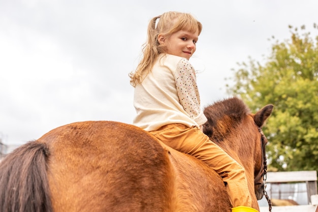 Niña montando pony sin montura, vista trasera de la gente por detrás